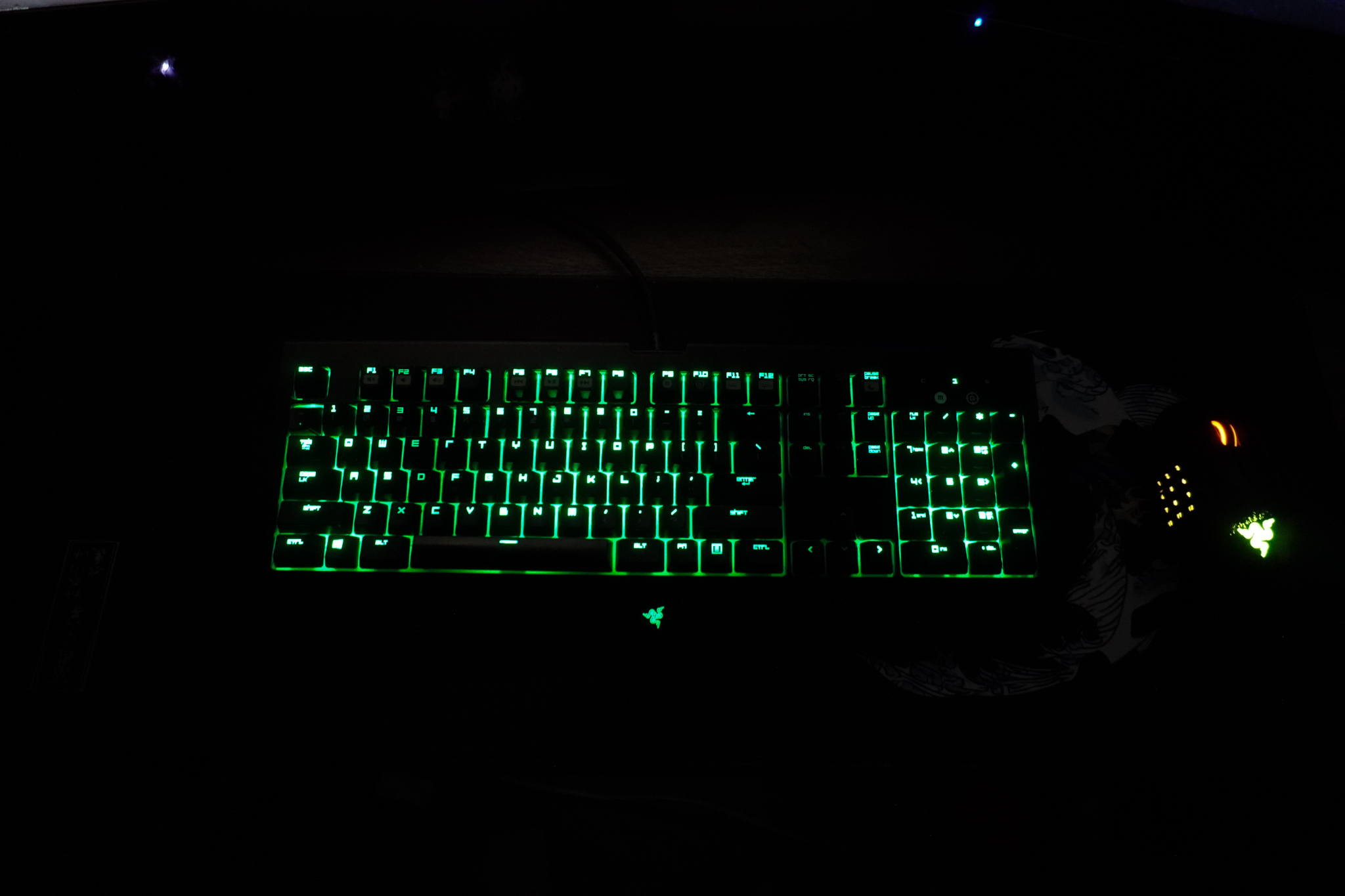Full-size Razer BlackWidow Ultimate 2016 keyboard with green backlighting in low light, with a mouse to its right.